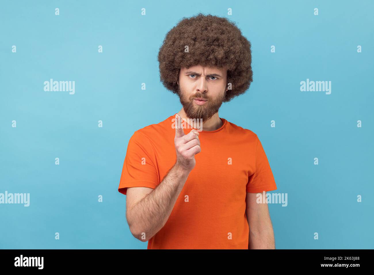 Portrait d'un homme sérieux avec une coiffure afro portant un T-shirt orange debout avec un geste d'admonishing, en faisant des signes d'erreur et d'avertissement. Studio d'intérieur isolé sur fond bleu. Banque D'Images