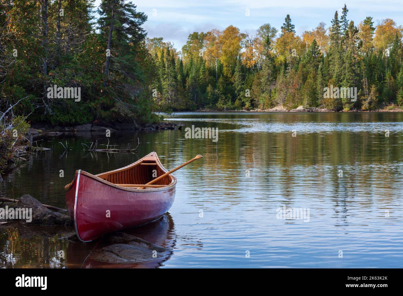 Canoë en bois rouge sur la rive d'un lac Boundary Waters dans la lumière du matin pendant l'automne Banque D'Images