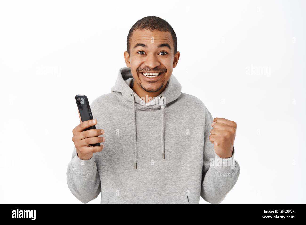 Homme enthousiaste tenant un téléphone portable et une carte de crédit, célébrant la victoire sur smartphone, gagnant sur téléphone, debout sur fond blanc Banque D'Images