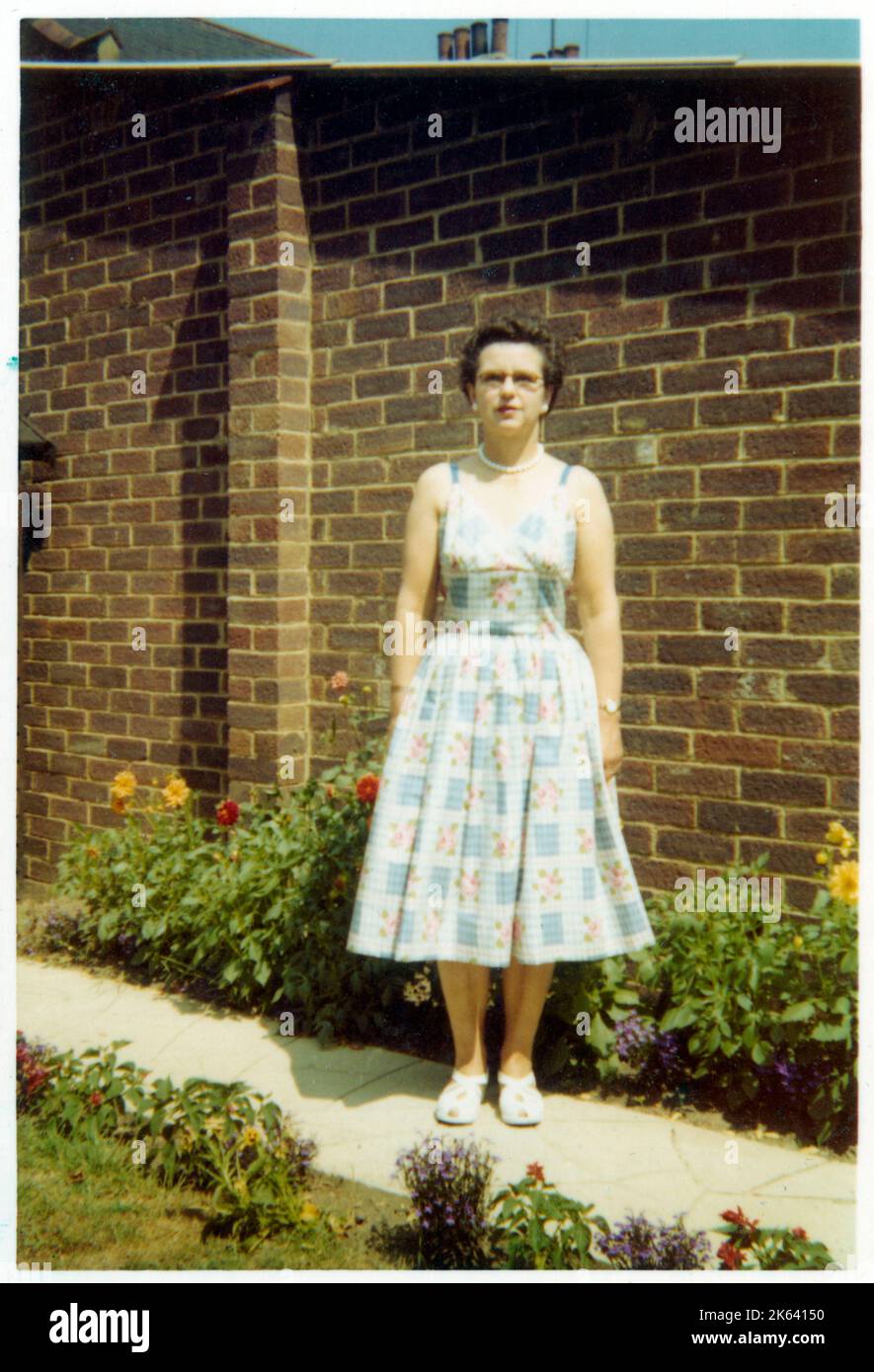 Une femme d'âge moyen debout (très!) Envolez-vous sur un sentier le long d'un magnifique jardin fleuri suburbain arrière - août 1959 Banque D'Images