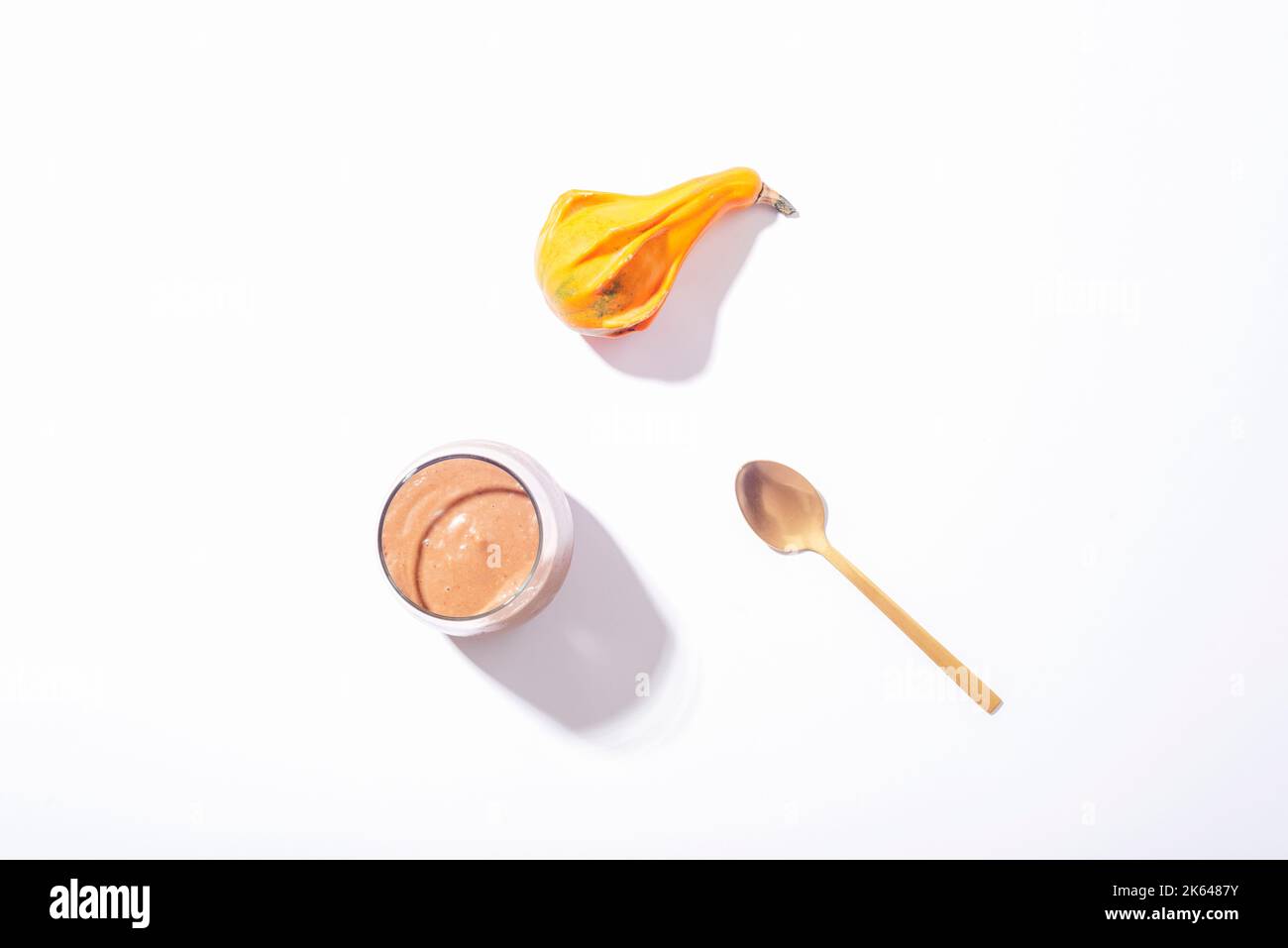 Verre avec smoothie au chocolat avec cuillère et citrouille d'orange sur fond blanc. Concept d'automne. Une alimentation saine. Vue de dessus, plan d'appartement Banque D'Images