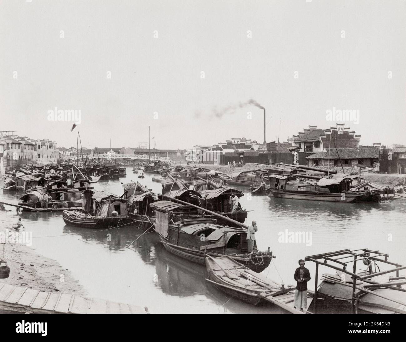 Photo du XIXe siècle : rivière pleine de petits bateaux, cheminée d'usine en arrière-plan, scène urbaine animée, Asie. Banque D'Images