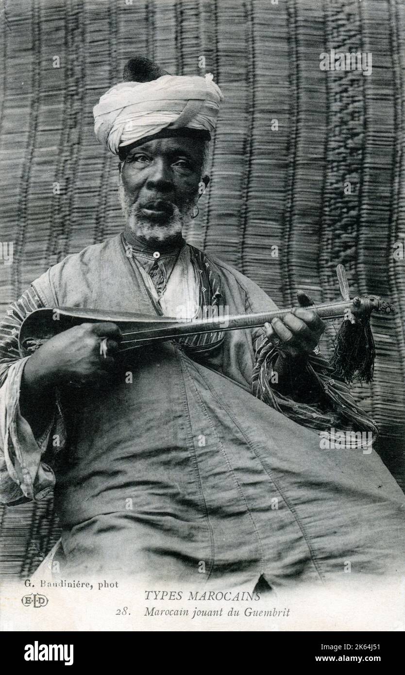 Un vieil homme marocain jouant un sintir, également connu sous le nom de guembri, gimbri ou hejhouj, est un luth pincé de basse à trois cordes recouvert de peau utilisé par le peuple Gnawa. Il est approximativement de la taille d'une guitare, avec un corps sculpté dans une bûche et recouvert sur le côté de jeu de peau de chameau. Banque D'Images