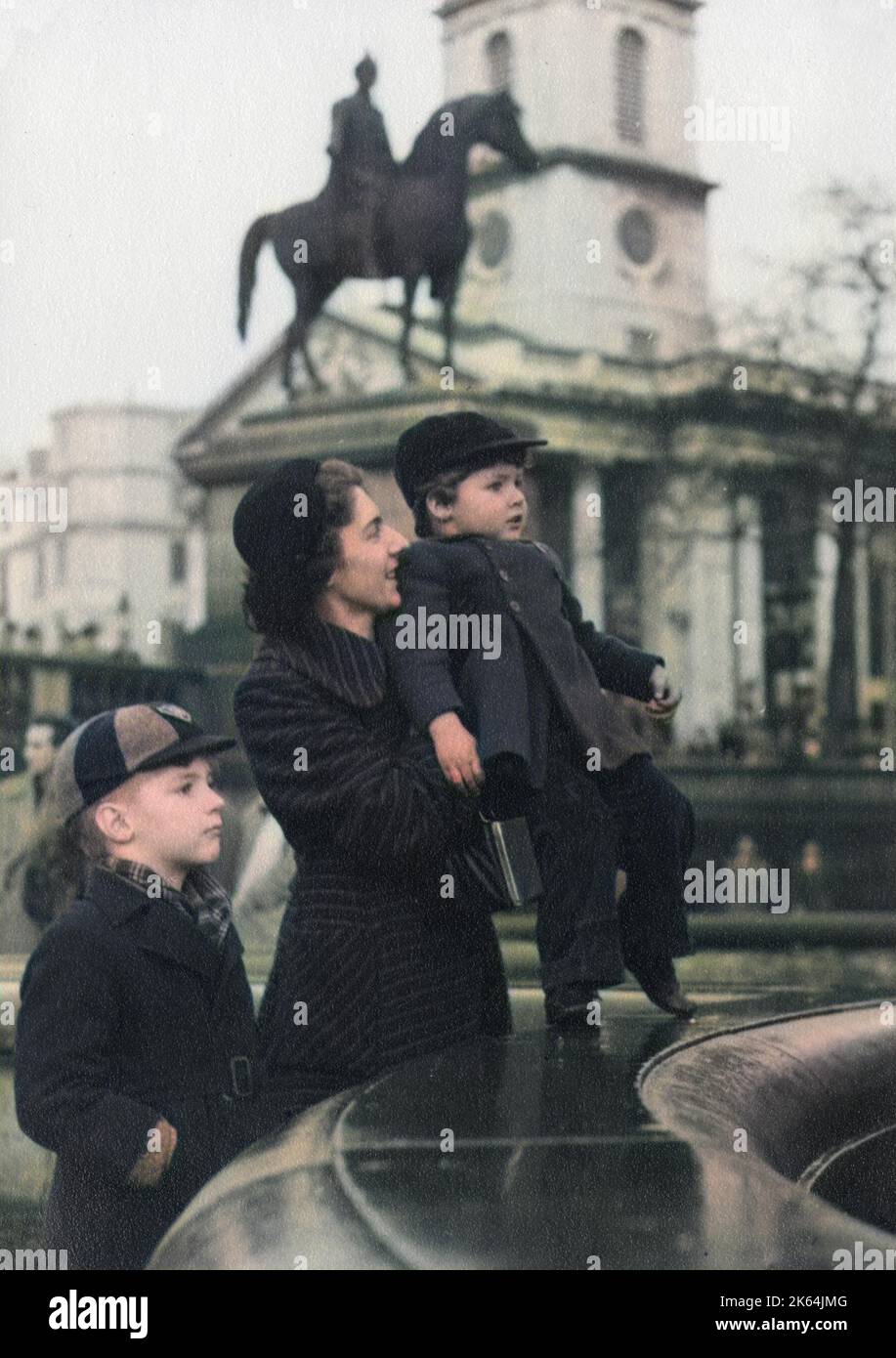 Une délicieuse photographie d'une mère et ses deux garçons par l'une des fontaines de Trafalgar Square, Londres - années 1950 La forme distinctive de l'église de St Martin-in-the-Fields peut être vue en arrière-plan, derrière la statue du roi George IV à cheval. Banque D'Images