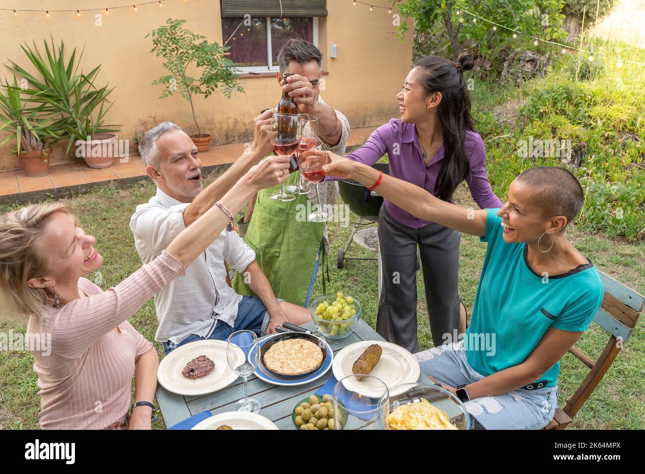 Un groupe d'amis joyeux qui toasent avec un grand sourire autour de la table au patio de la maison. Banque D'Images