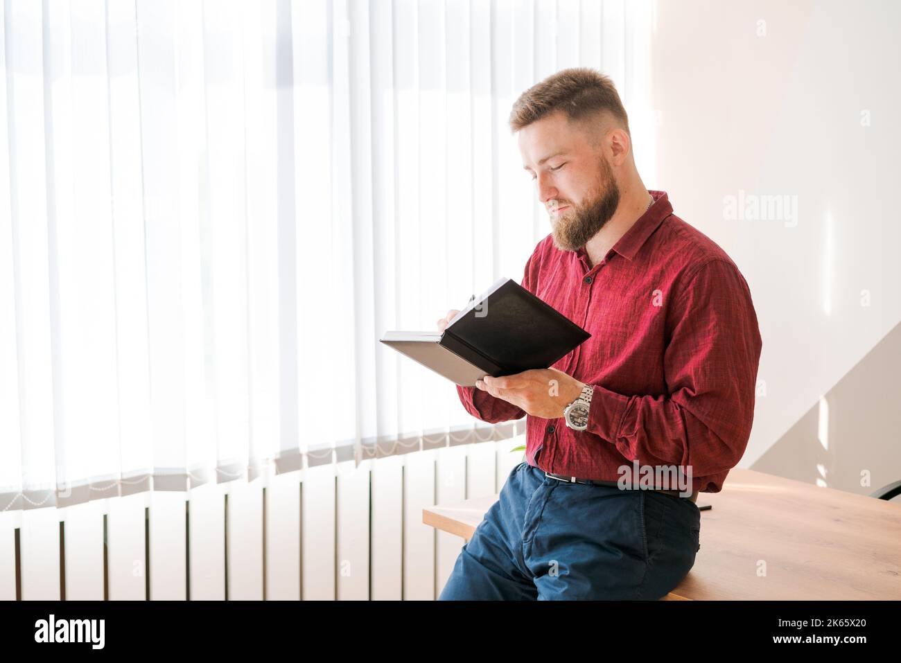 Les planificateurs planifient le calendrier et les rappels d'ordre du jour, les travaux de bureau. Un homme barbu a l'intention de se réunir tous les jours et d'écrire son voyage d'affaires dans un journal à la réception. Concept d'événement de rappel de calendrier. Banque D'Images