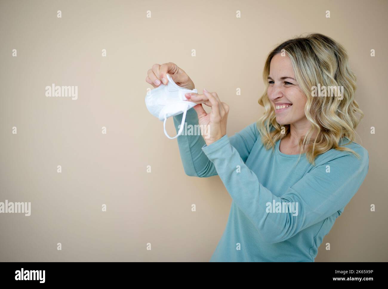 jolie jeune femme aux cheveux blonds bouclés portant ffp2 masque de protection devant un fond marron dans le studio Banque D'Images