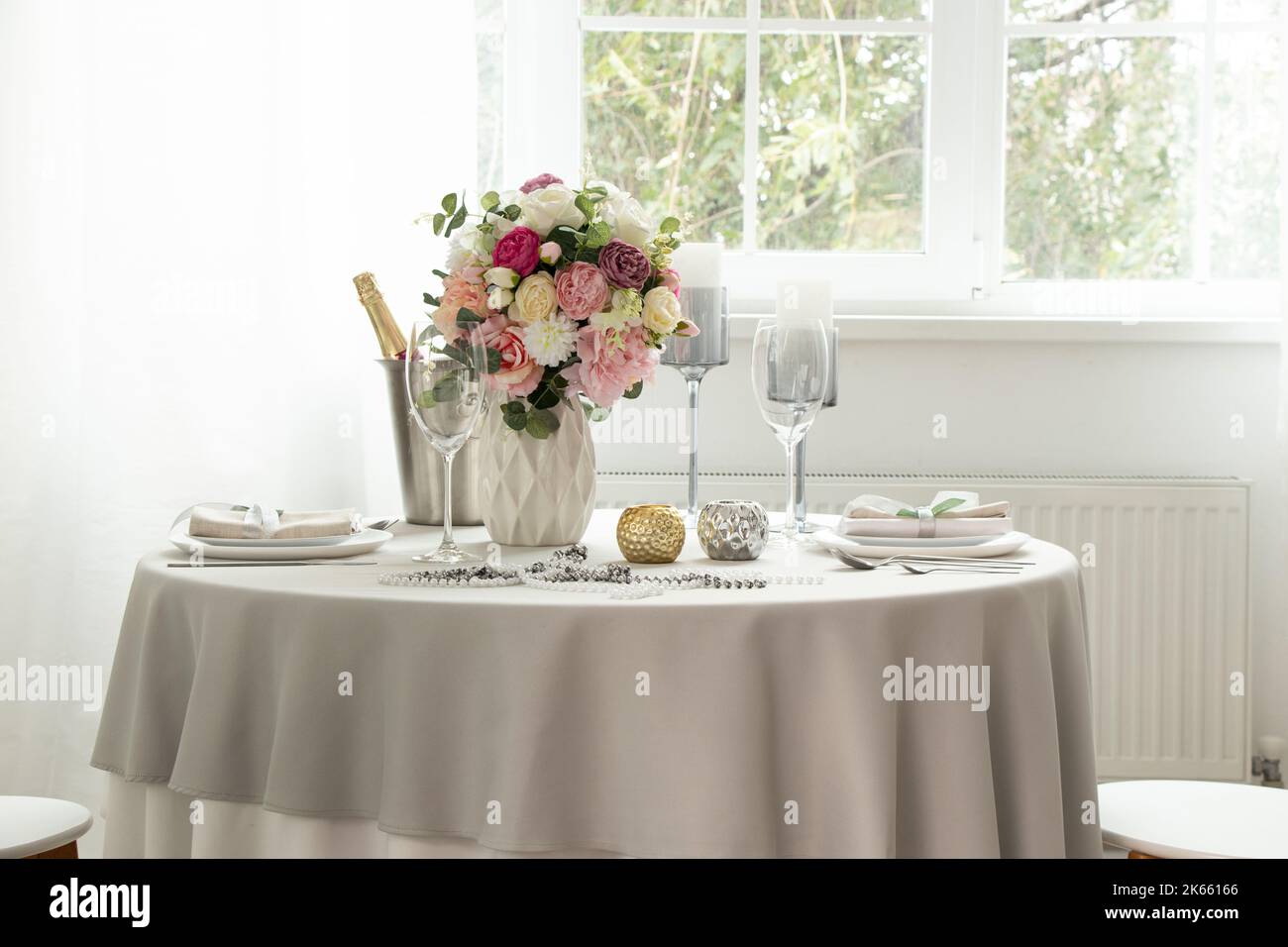 Une table de fête avec des plats de service et un seau de champagne dans un appartement près d'une fenêtre avec des murs blancs, un cadre de table de mariage Banque D'Images