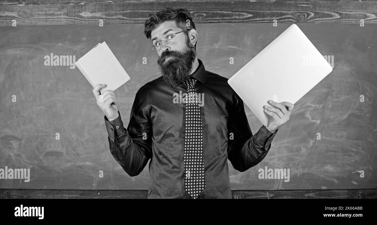 Restez moderne grâce à la technologie. Un hipster barbu pour enseignants tient un livre et un ordinateur portable. Les technologies modernes en bénéficient. Numérique contre papier. Choisissez le bon enseignement Banque D'Images