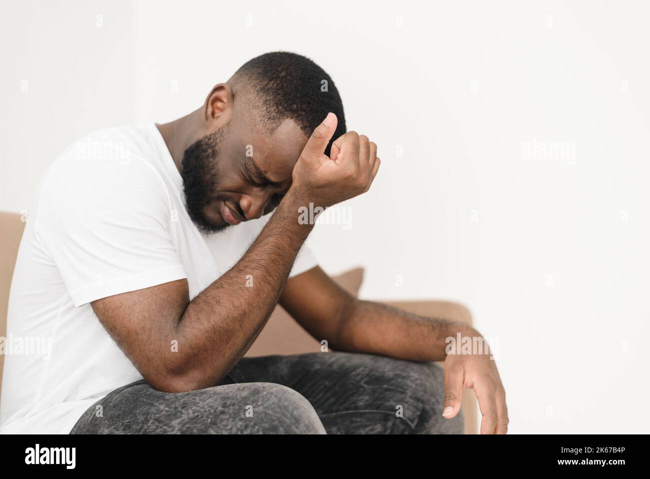 Homme afro-américain barbu stressé souffrant de maux de tête et assis sur un canapé à la maison et frottant son front, copier l'espace. Homme contrarié souffrant fr Banque D'Images