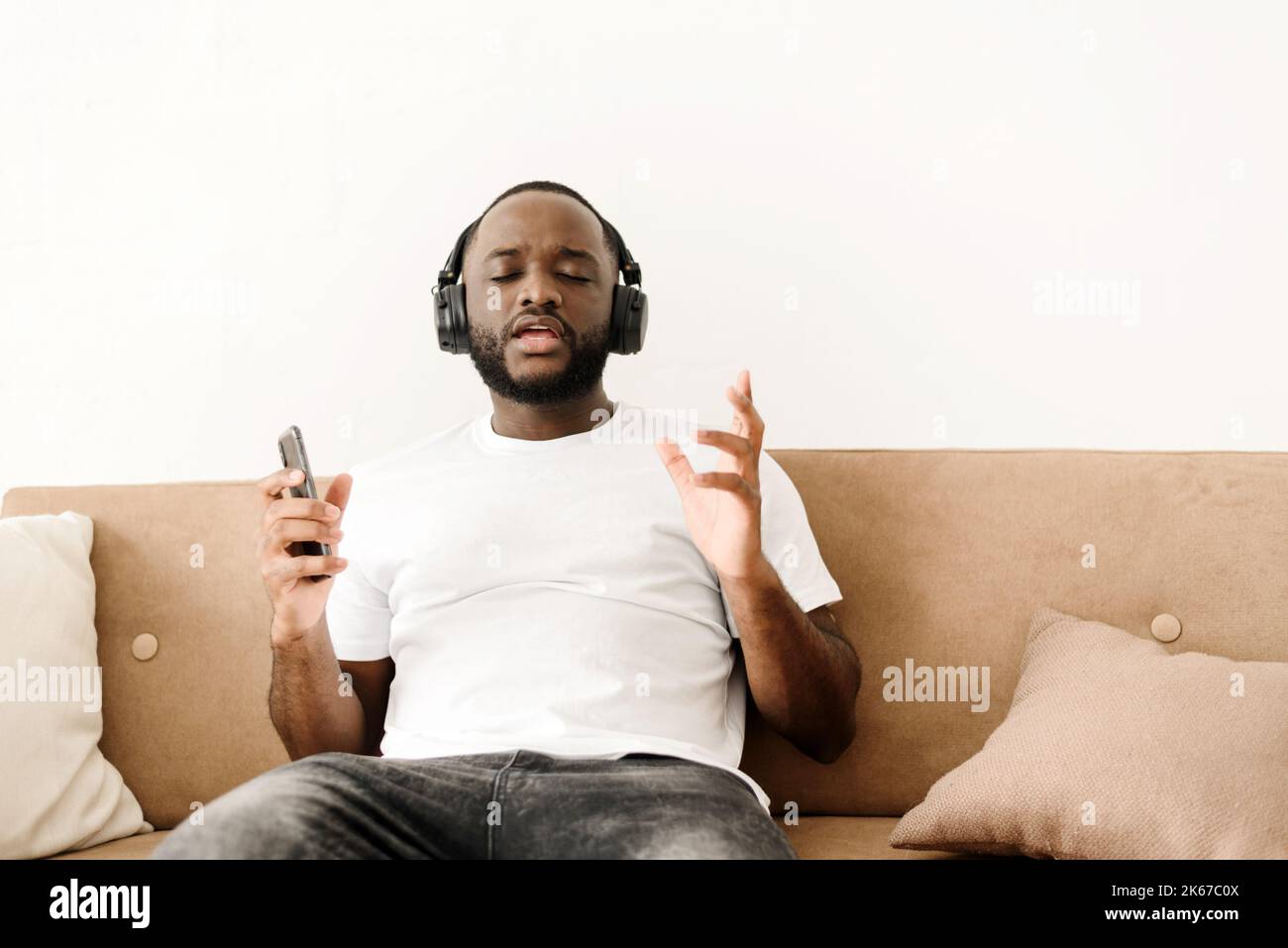 Portrait d'un jeune homme afro-américain appréciant écouter de la bonne musique à la maison, assis sur le canapé. Banque D'Images