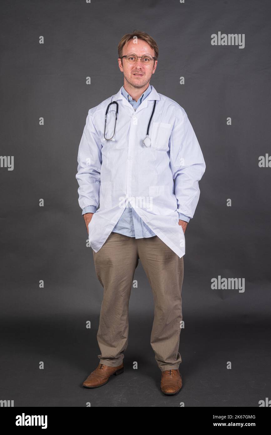 Prise de vue en longueur d'un médecin mâle avec stéthoscope au-dessus du cou dans un manteau médical sur fond gris prise verticale Banque D'Images