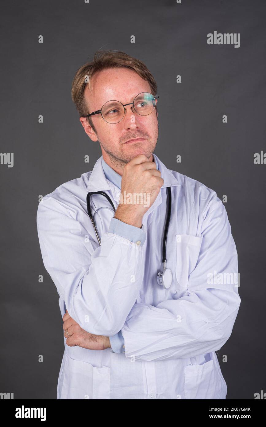 Médecin masculin sérieux avec stéthoscope au-dessus du cou dans la pensée médicale de manteau et la recherche verticale de tir Banque D'Images