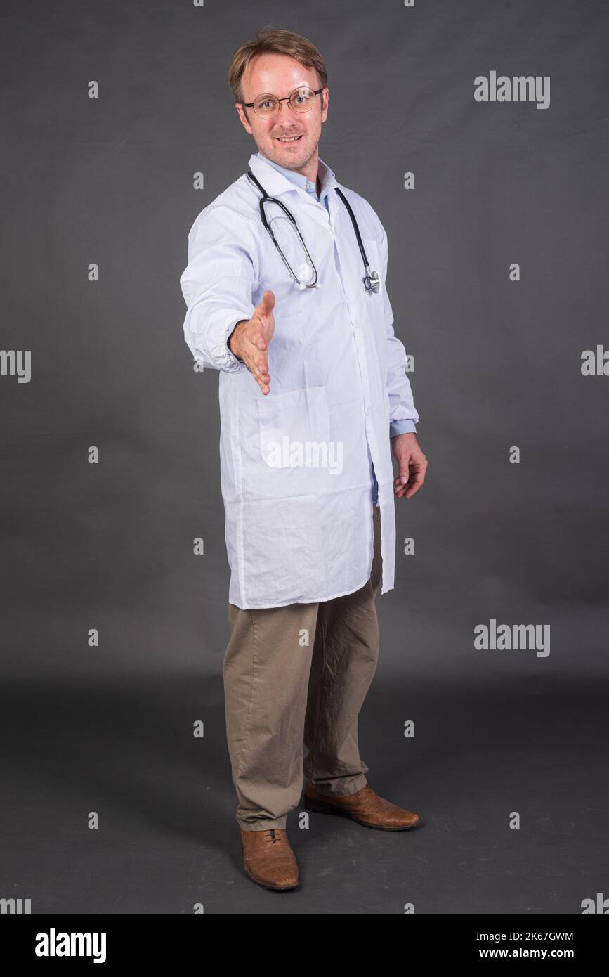 Souriant médecin avec stéthoscope sur le cou dans un manteau médical offrant poignée de main sur fond gris tir vertical Banque D'Images