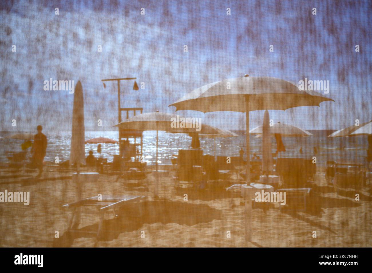 Scène de plage avec des baigneurs de soleil et des parasols photographiés à travers un écran en maille à la plage de Sottovento près de Gallipoli, Apulia (Puglia), Italie. Banque D'Images