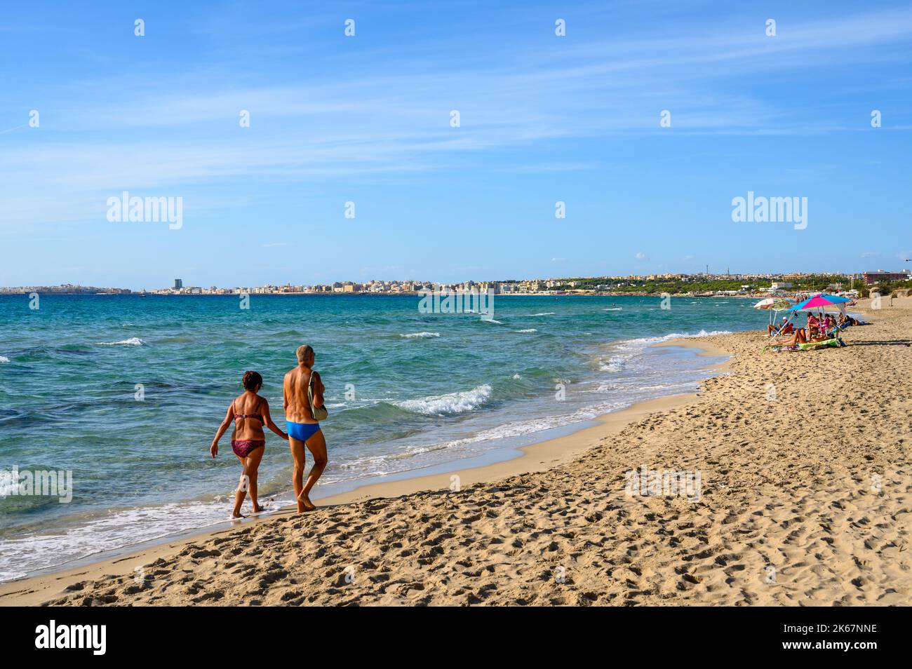 Vue sur la baie à Gallipoli ville de Sottovento plage avec un couple âgé marchant sur le sable, Apulia (Puglia), Italie. Banque D'Images