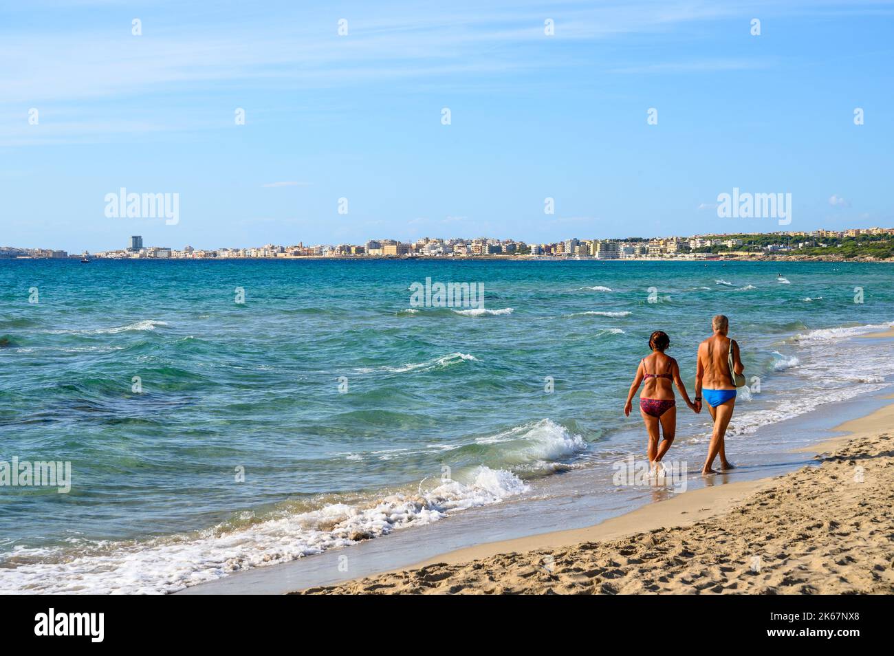 Vue sur la baie à Gallipoli ville de Sottovento plage avec un couple âgé marchant sur le sable, Apulia (Puglia), Italie. Banque D'Images