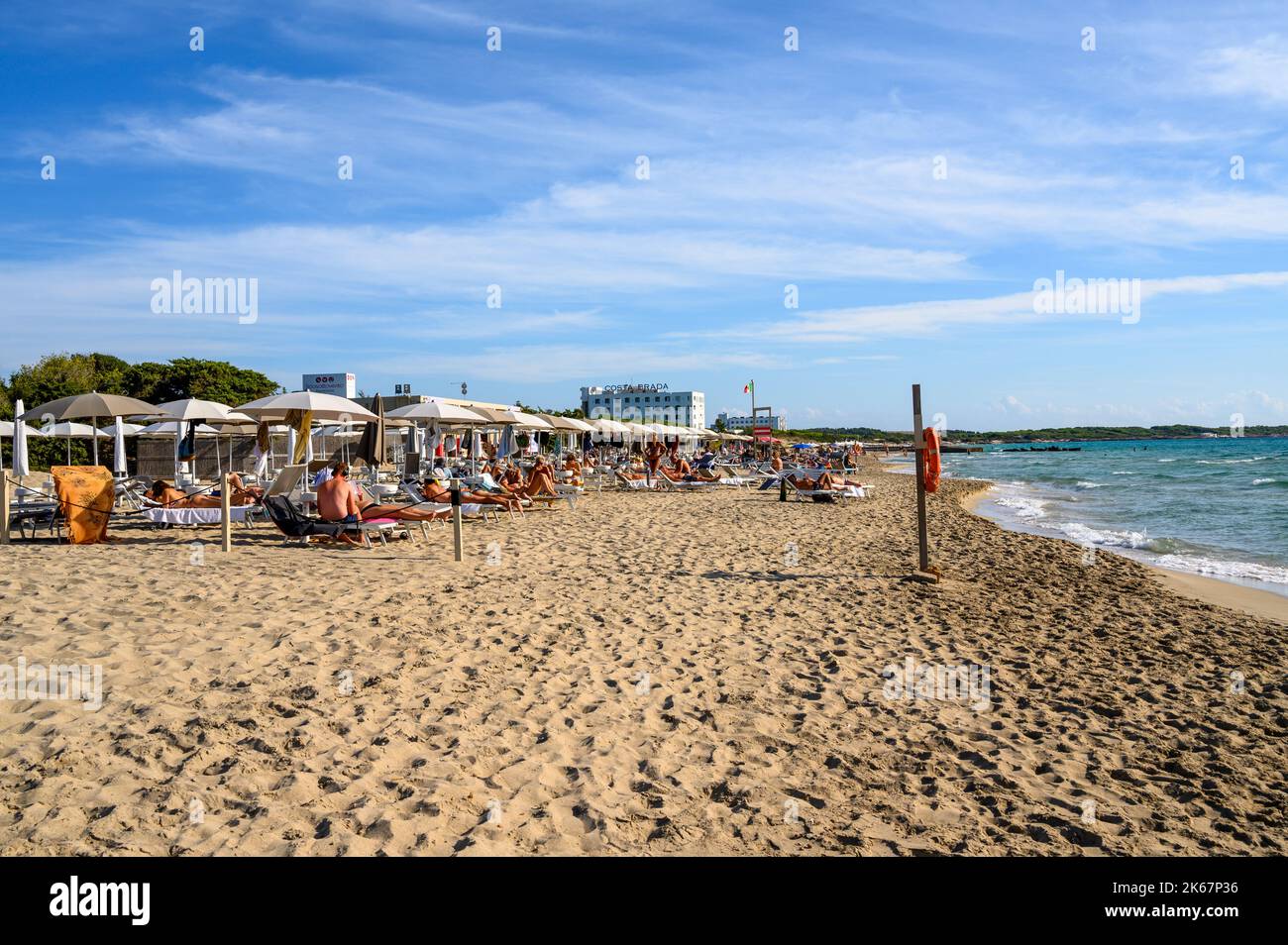 Vue sud sur la plage de Sottovento vers l'hôtel Costa Brada avec des personnes, des chaises longues et des parasols près de Gallipoli, Apulia (Puglia), Italie. Banque D'Images