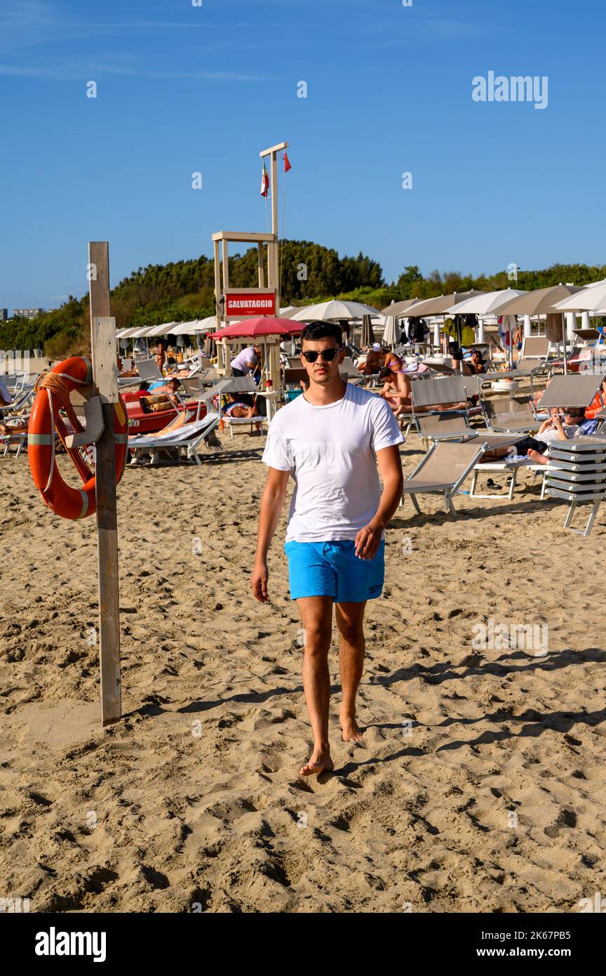 Un jeune homme de race mixte dans ses années vingt marche vers l'appareil photo sur la plage de Sottovento au sud de Gallipoli à Apulia (Puglia), Italie. Banque D'Images