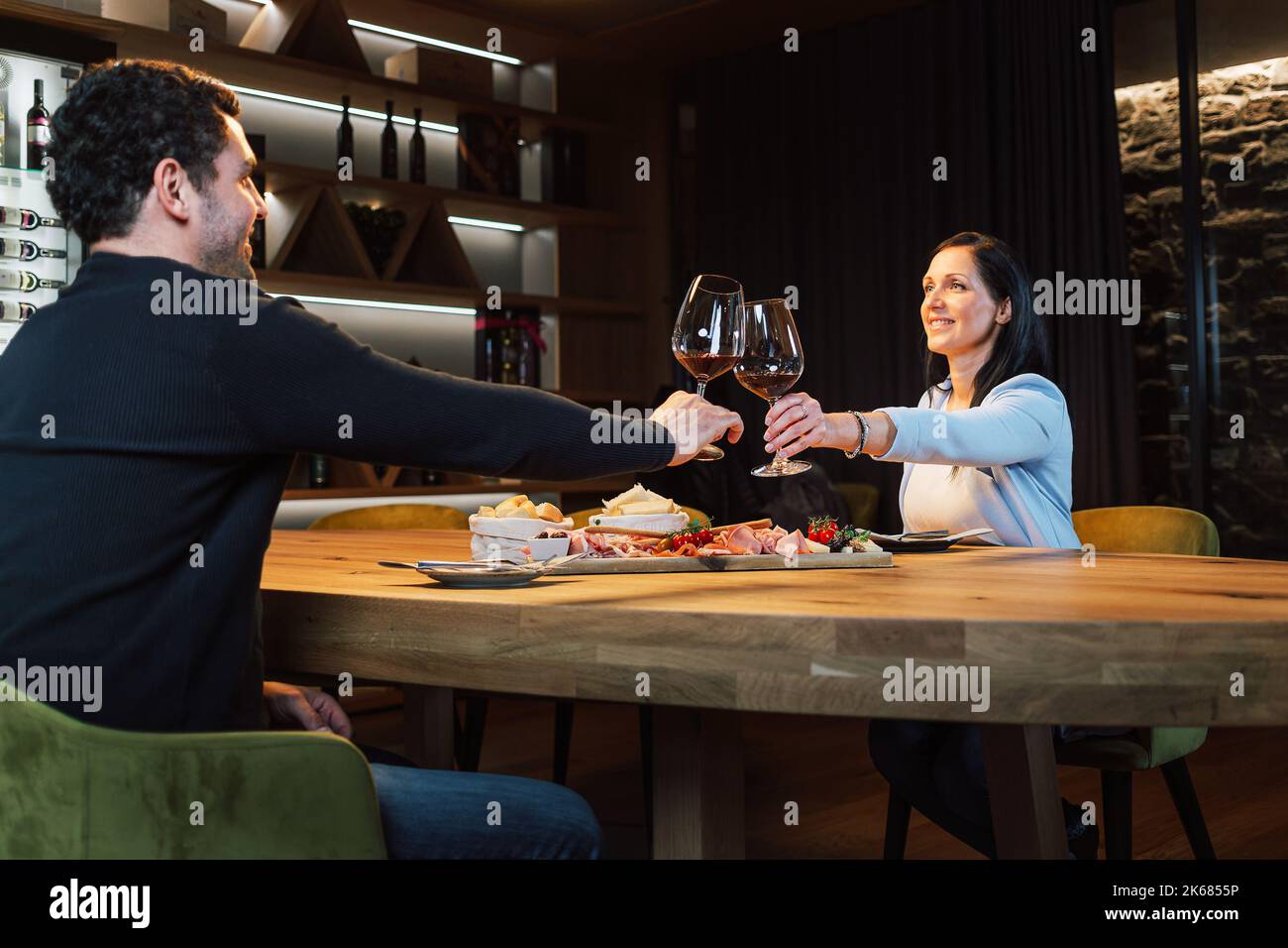 Couple romantique assis l'un en face de l'autre à la table à manger dans la salle à vin, des verres à vin et un verre de vin blanc Banque D'Images