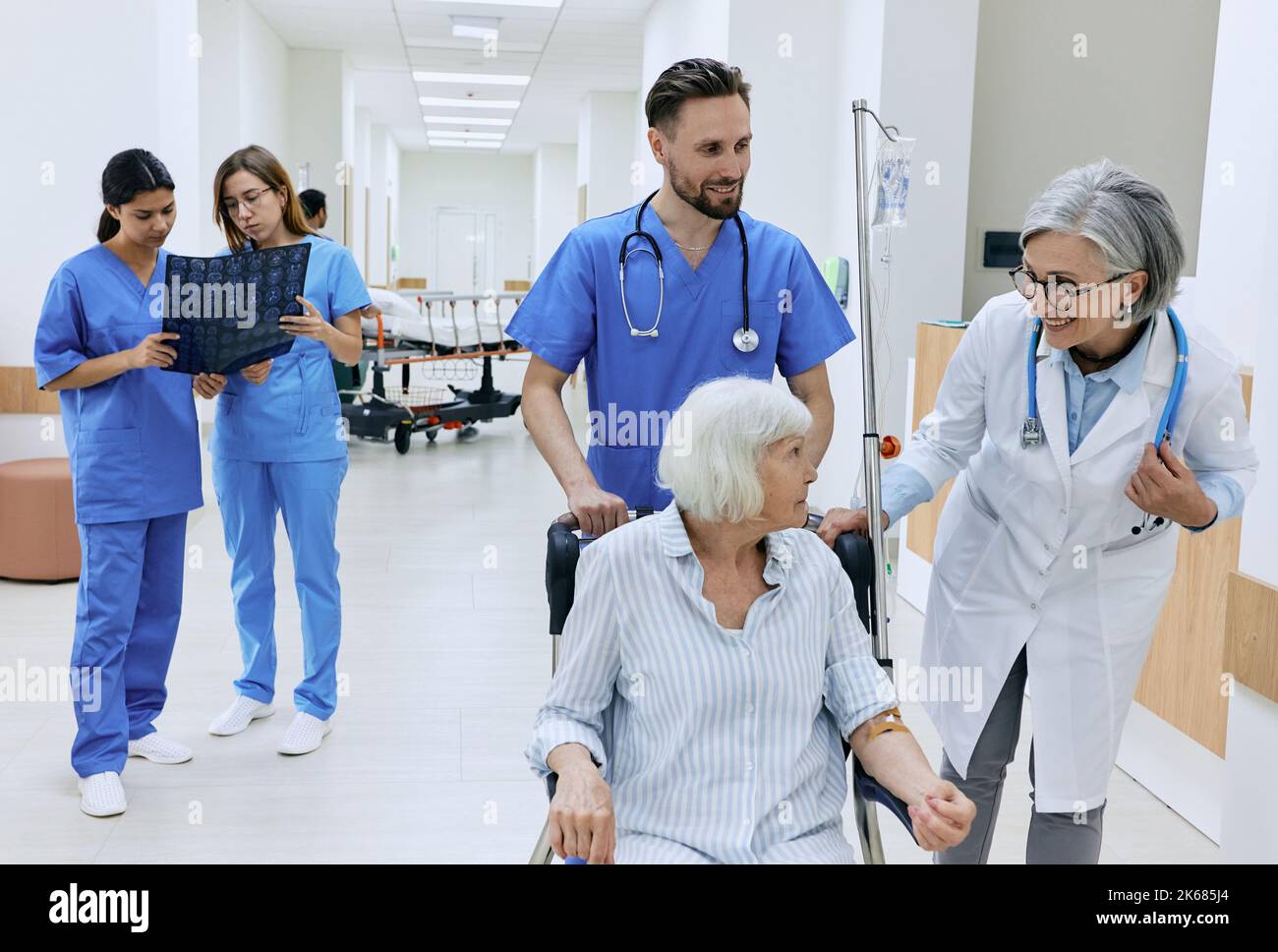 Amical médecin et infirmière prennent soin de la santé de la femme âgée assise sur un fauteuil roulant médical avec compte-gouttes intraveineux dans sa main. soins aux patients en hosp Banque D'Images