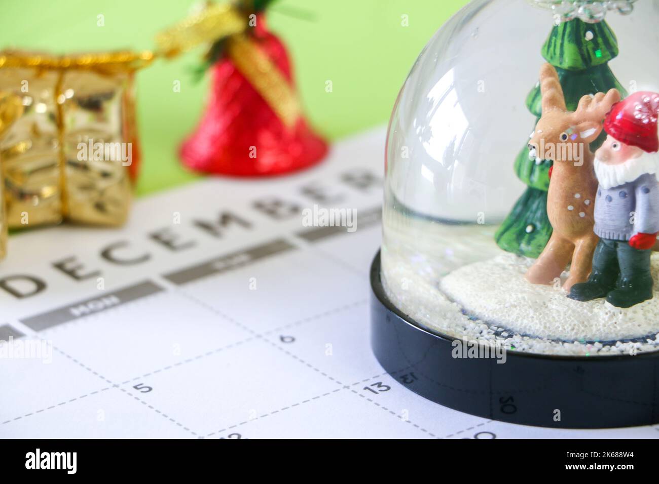 Concept de l'heure de Noël, gros plan du globe de neige festif sur le calendrier de décembre, cadeau de Noël et cloche en arrière-plan, mise au point sélective Banque D'Images