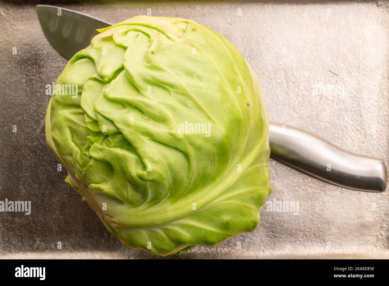 Une tête de chou naturel vert vif avec un couteau en métal, gros plan, sur un plateau en métal, vue du dessus. Banque D'Images