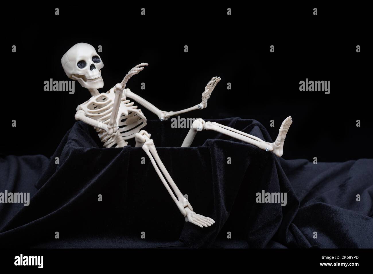 Un squelette de jouet rampant hors de la tombe et agitant, saluant sur un fond noir. Carte de voeux pour Halloween. Banque D'Images