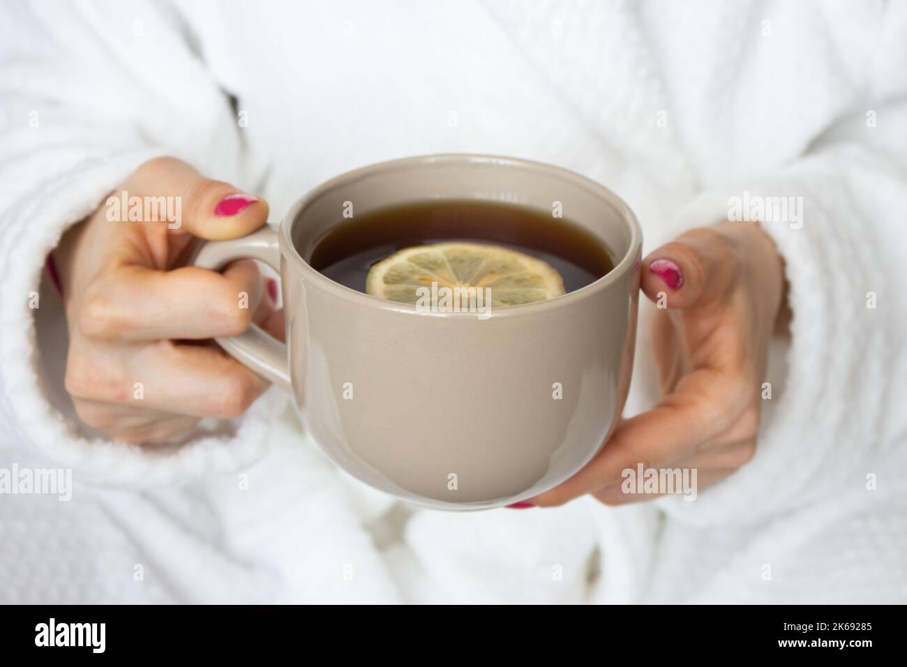 Femme tenant une tasse de thé avec du citron. Fille en peignoir blanc tenant une tasse de thé brune. Concept de confort à domicile. Concept boisson du matin. Détente et confort. Banque D'Images