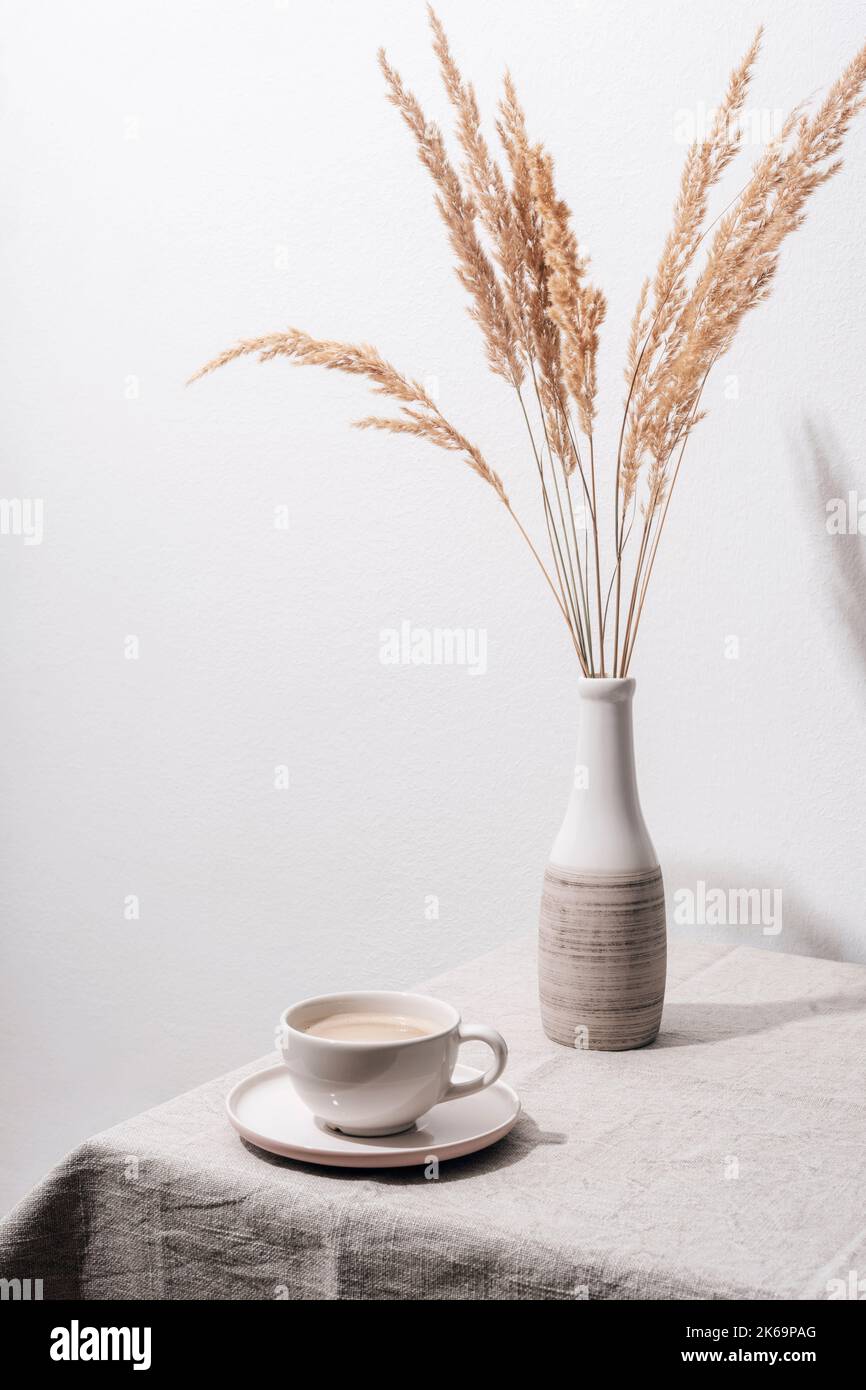 Une tasse de café et un vase avec de l'herbe de pampas sur une table avec nappe. Encore la vie. Banque D'Images
