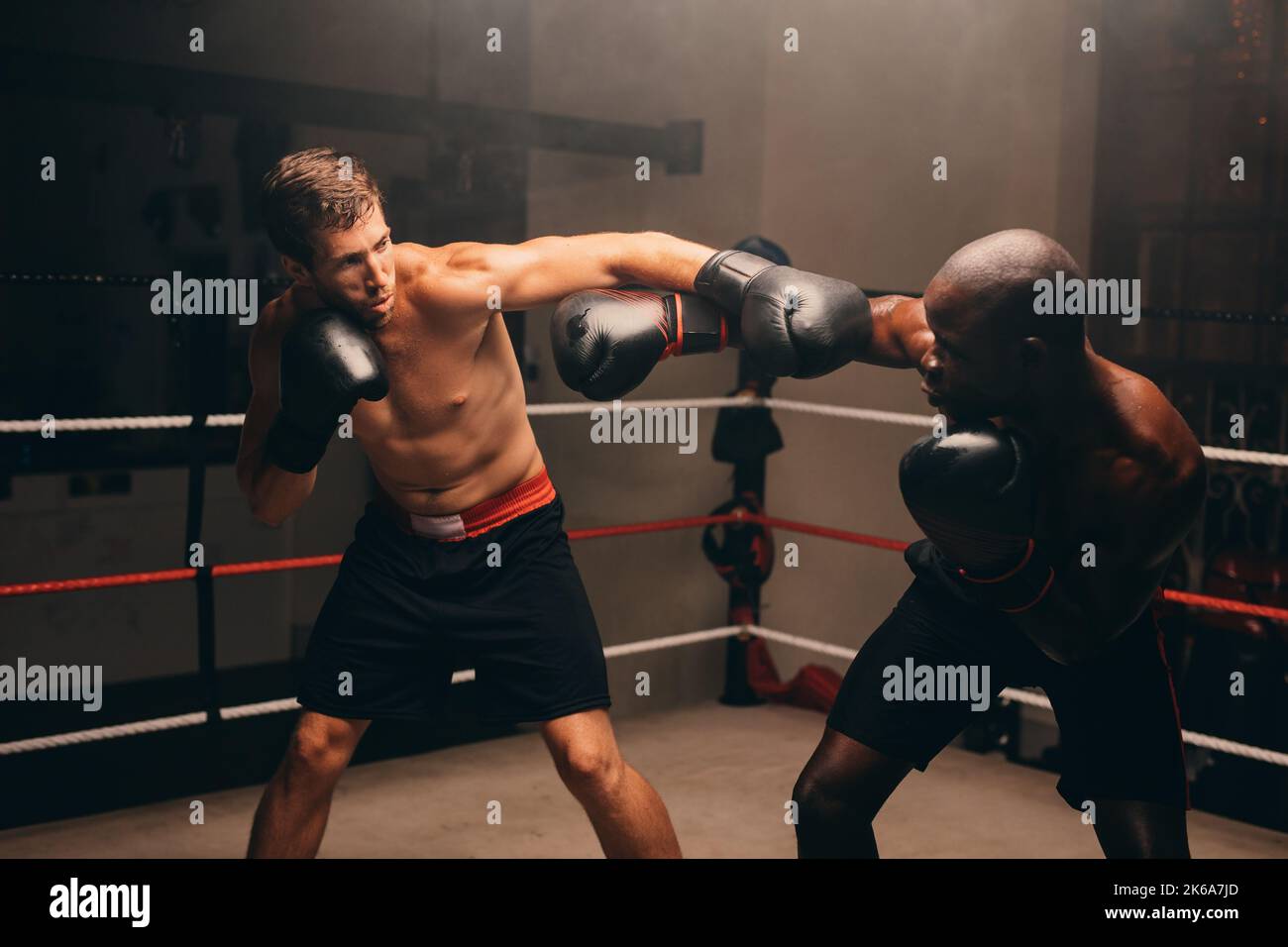 Des boxeurs mâles se lancent des coups de poing l'un contre l'autre lors d'un combat dans un ring de boxe. Deux jeunes hommes sportifs ayant un match de boxe dans une salle de fitness. Banque D'Images