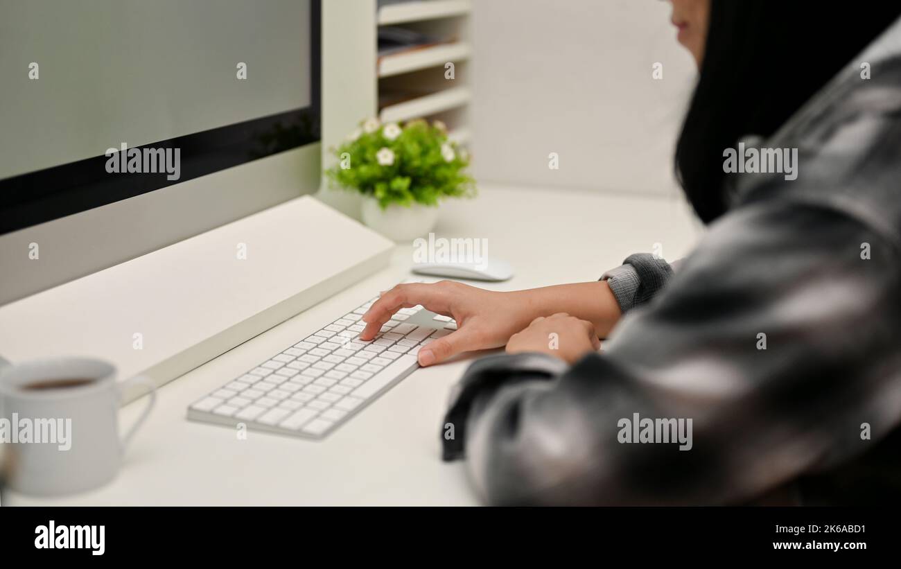 Vue arrière, Hipster femme graphiste ou programeuse en chemise en flanelle travaillant à son bureau, tapant sur le clavier d'ordinateur. Banque D'Images