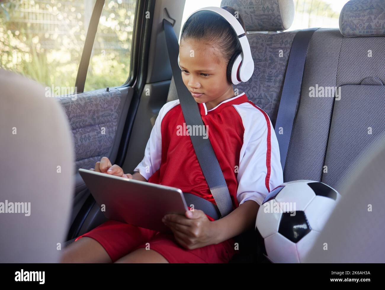 Tablette, sport et détente enfant en voiture transport au football, au football ou match dans une fourgonnette SUV avec ceinture de sécurité. Jeune fille streaming Banque D'Images