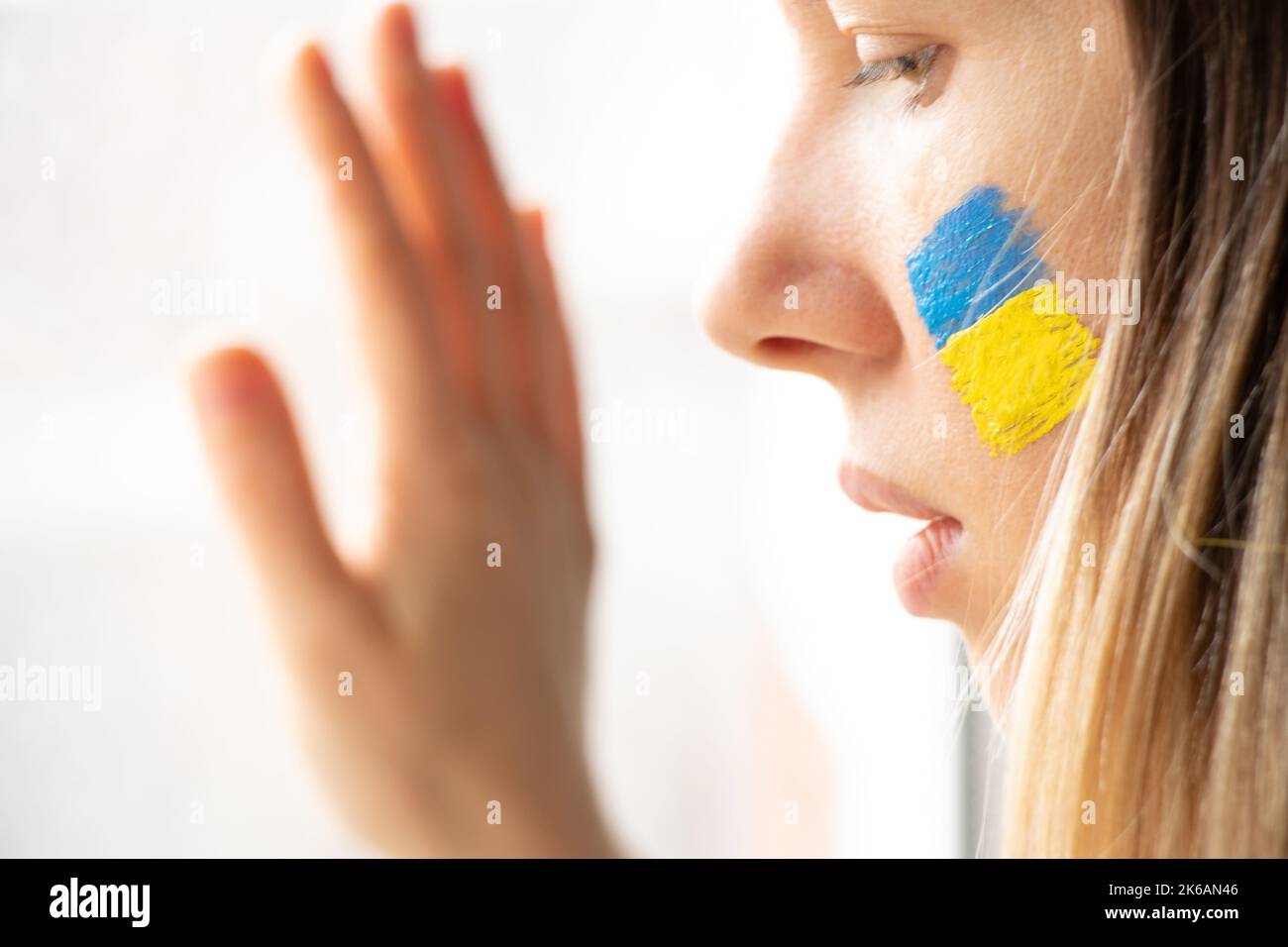 Une femme ukrainienne avec le drapeau national de l'Ukraine jaune-bleu sur son visage regarde par la fenêtre, patriote, la paix en Ukraine, la loi martiale, je vois la wa Banque D'Images