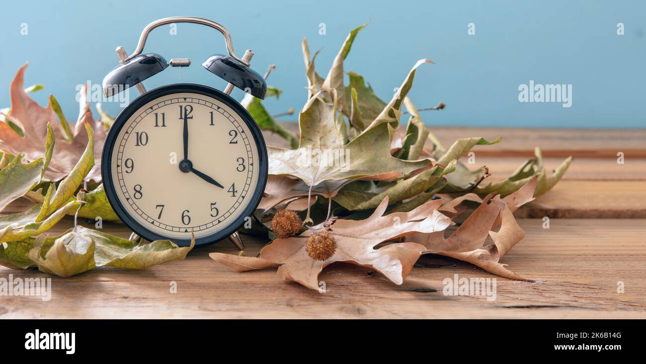 Heure d'été de retour. Réveil noir et feuilles d'automne sur table en bois, espace de copie Banque D'Images