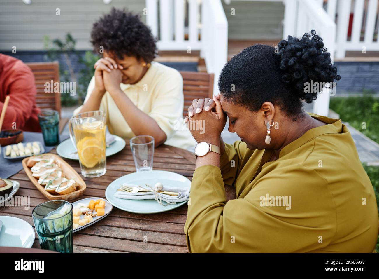 Vue latérale portrait de la jeune femme noire priant à la table à l'extérieur pendant la réunion de famille Banque D'Images