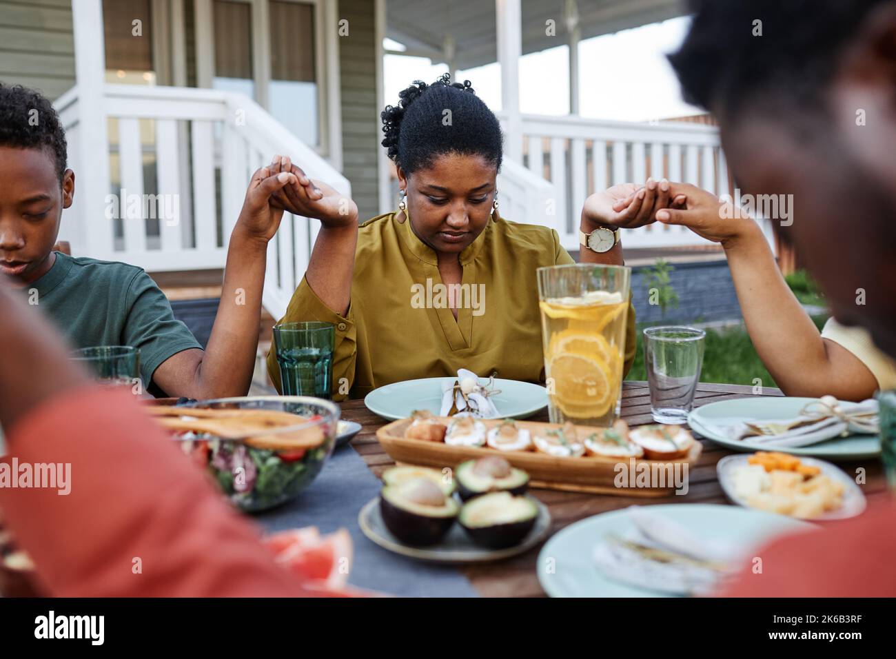 Portrait d'une jeune femme afro-américaine qui dit grâce à la table à l'extérieur pendant la réunion de famille et les mains Banque D'Images