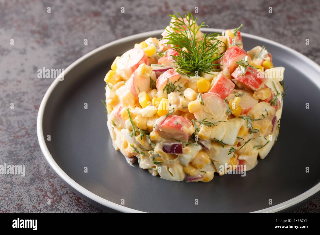 Salade épicée avec viande de crabe, maïs doux, oignon rouge, œufs durs et aneth dans l'assiette sur la table. Horizontale Banque D'Images