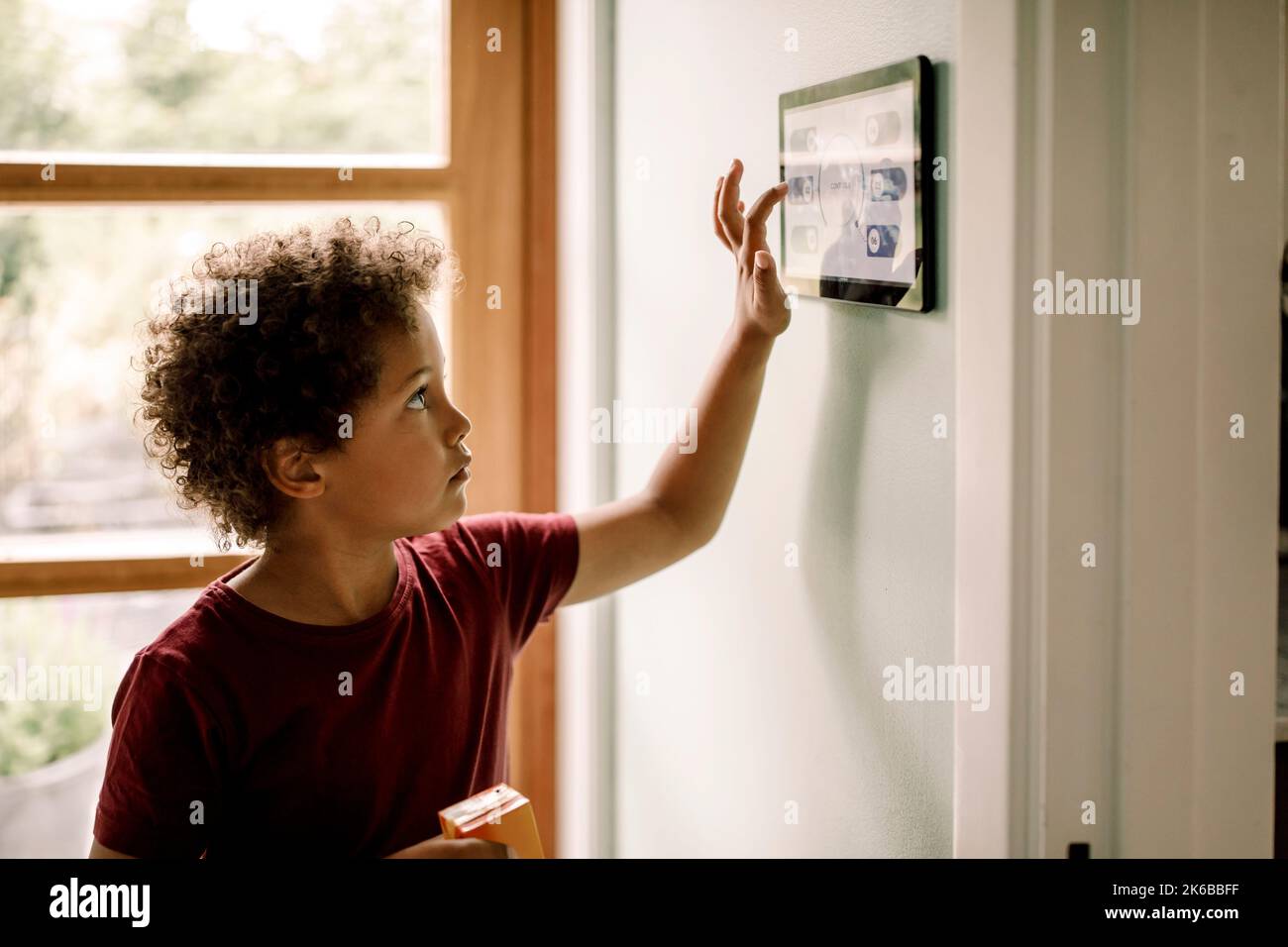 Garçon avec des cheveux bouclés à l'aide d'un système domotique monté au mur Banque D'Images