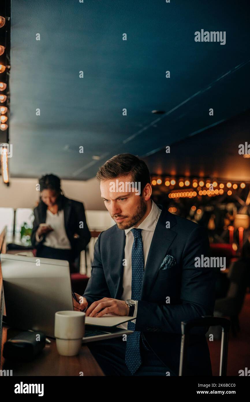 Jeune homme d'affaires utilisant un ordinateur portable tout en étant assis dans le salon de l'hôtel Banque D'Images