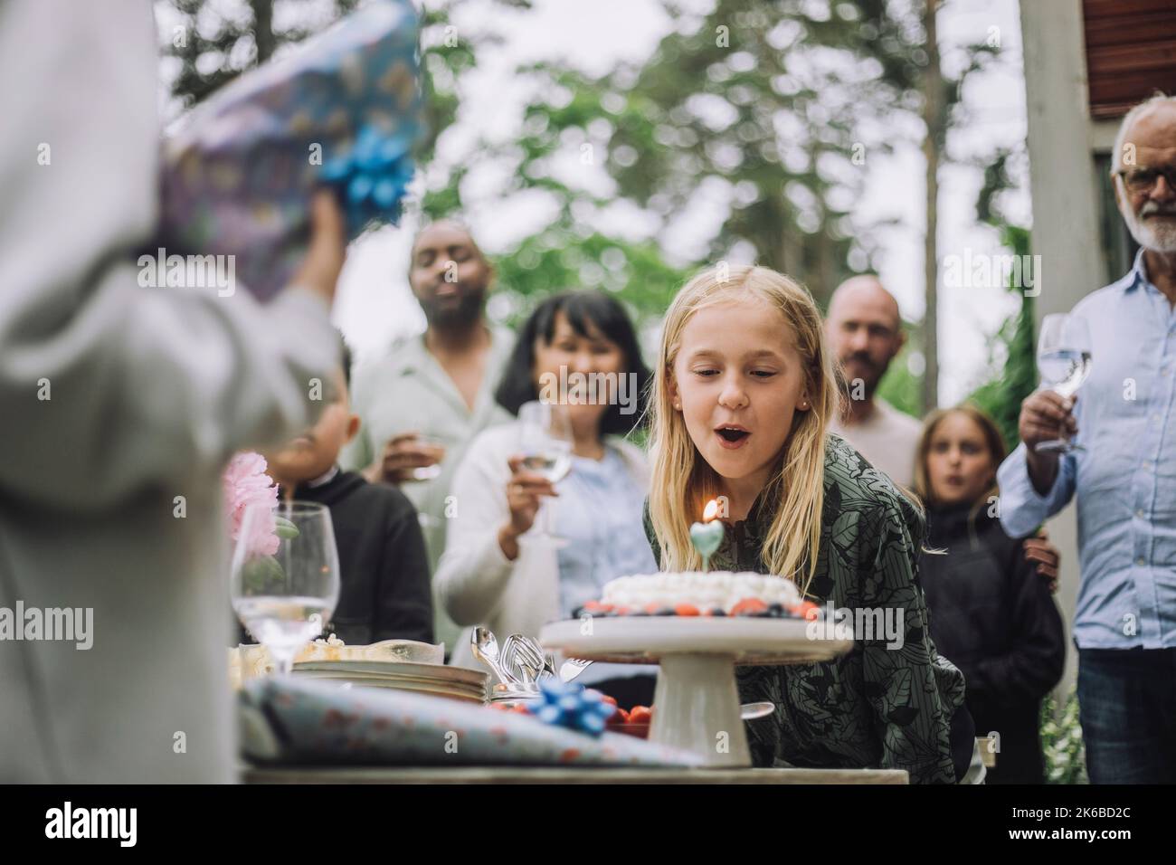 Bonne fille soufflant bougie sur le gâteau pendant la fête d'anniversaire avec la famille Banque D'Images