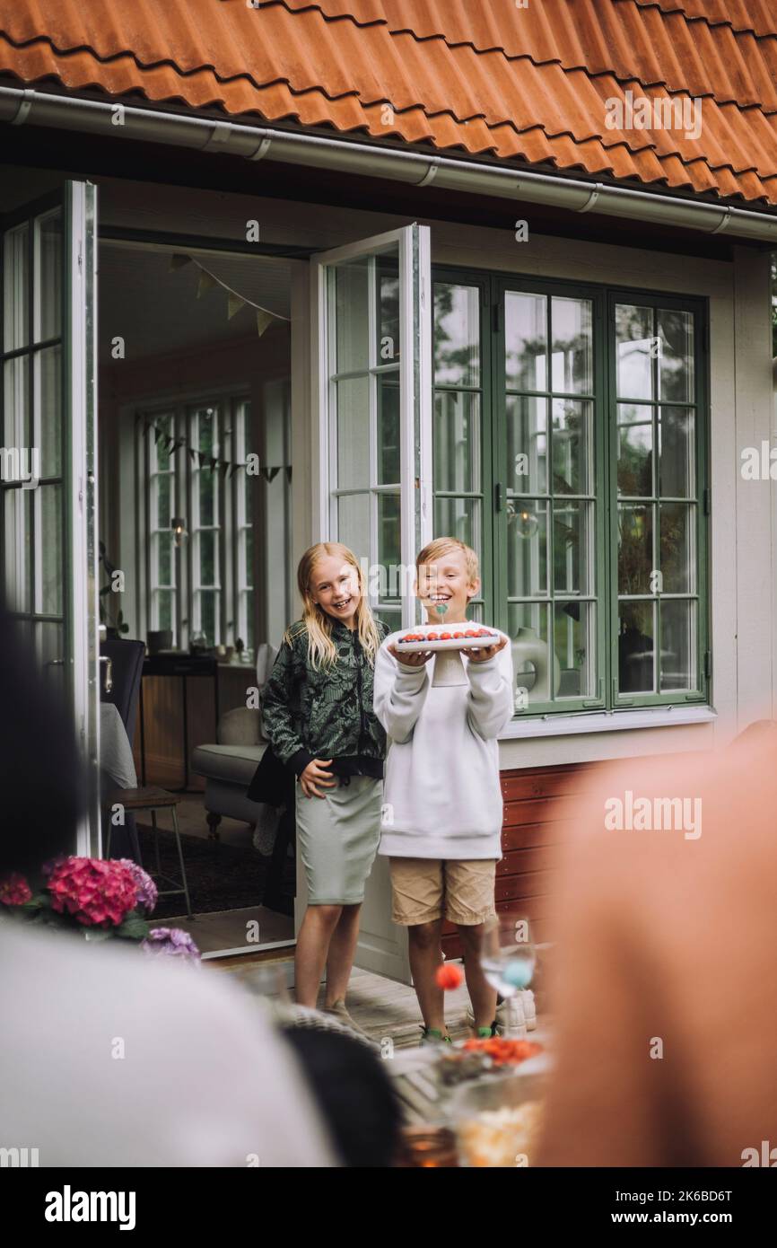 Fille debout avec un ami tenant un gâteau d'anniversaire près de la porte Banque D'Images