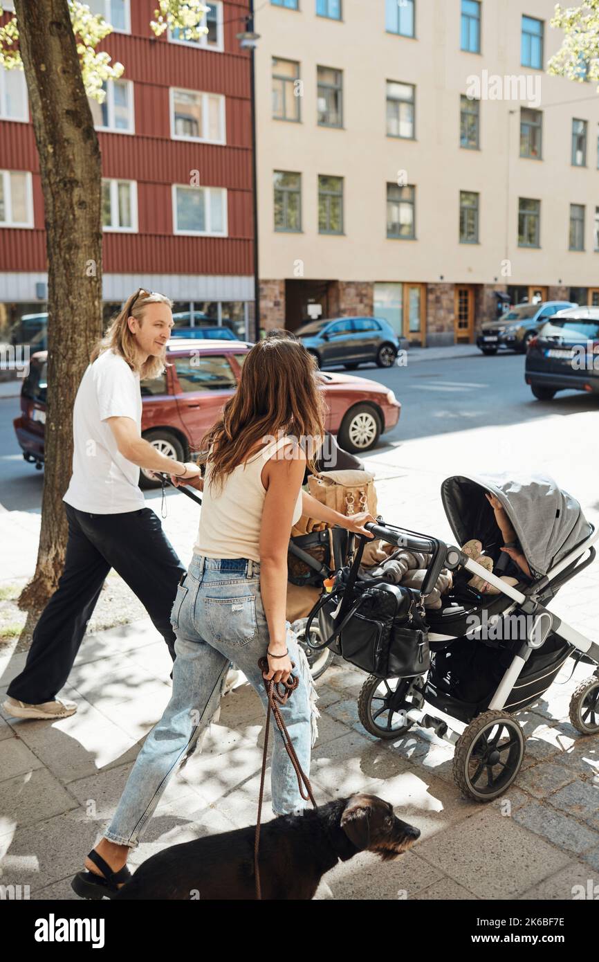 Homme et femme parlant en poussant les poussettes avec les enfants sur le trottoir Banque D'Images