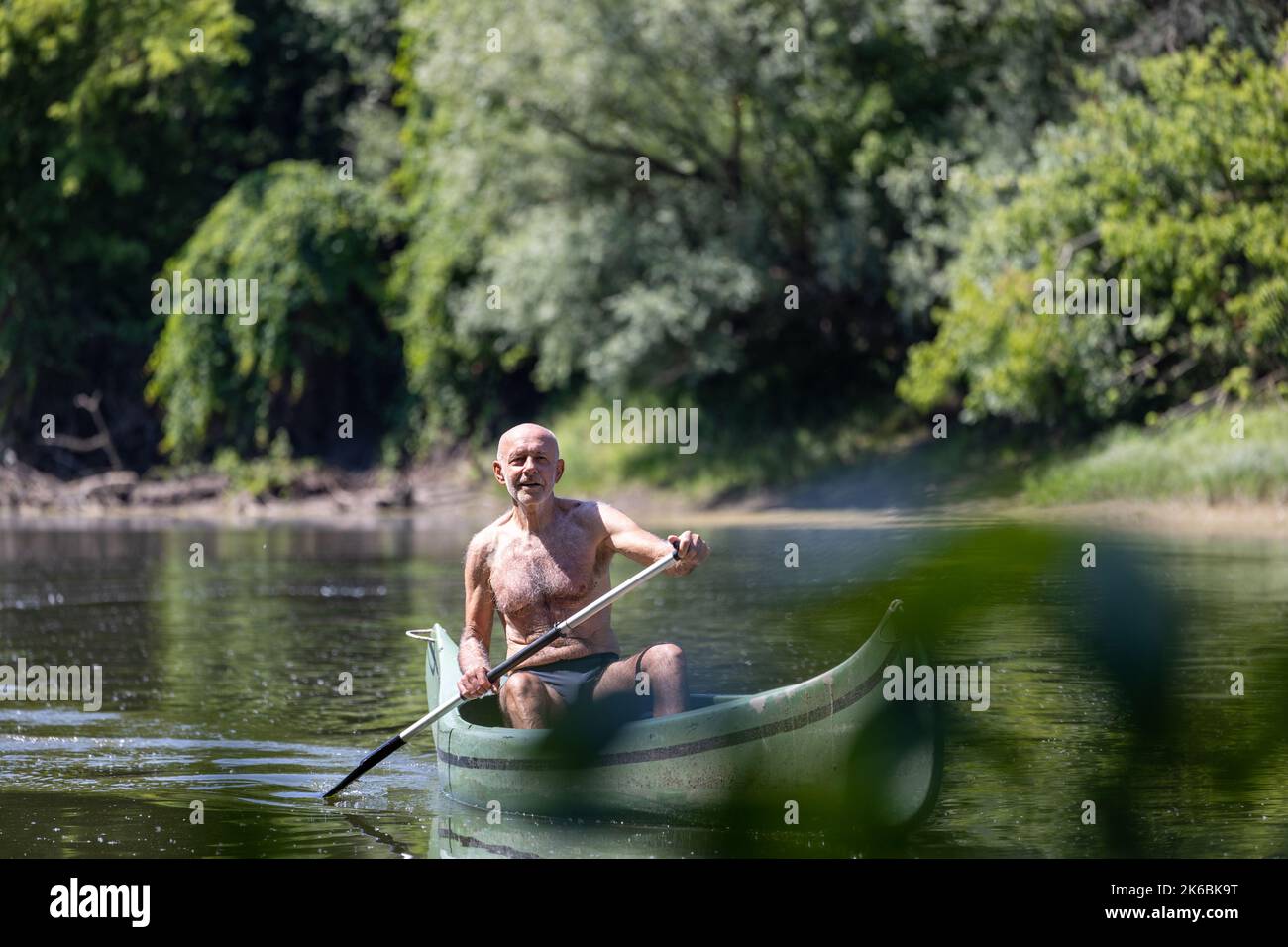 Homme senior heureux portant un maillot de bain en aviron en bateau à poissons sur la rivière en été Banque D'Images