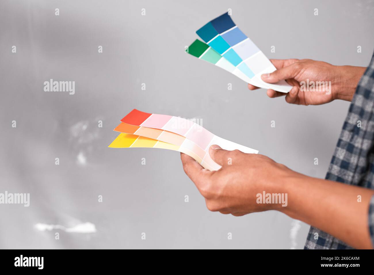 Gros plan des mains tenant les échantillons de peinture de couleur vive contre le mur gris Banque D'Images