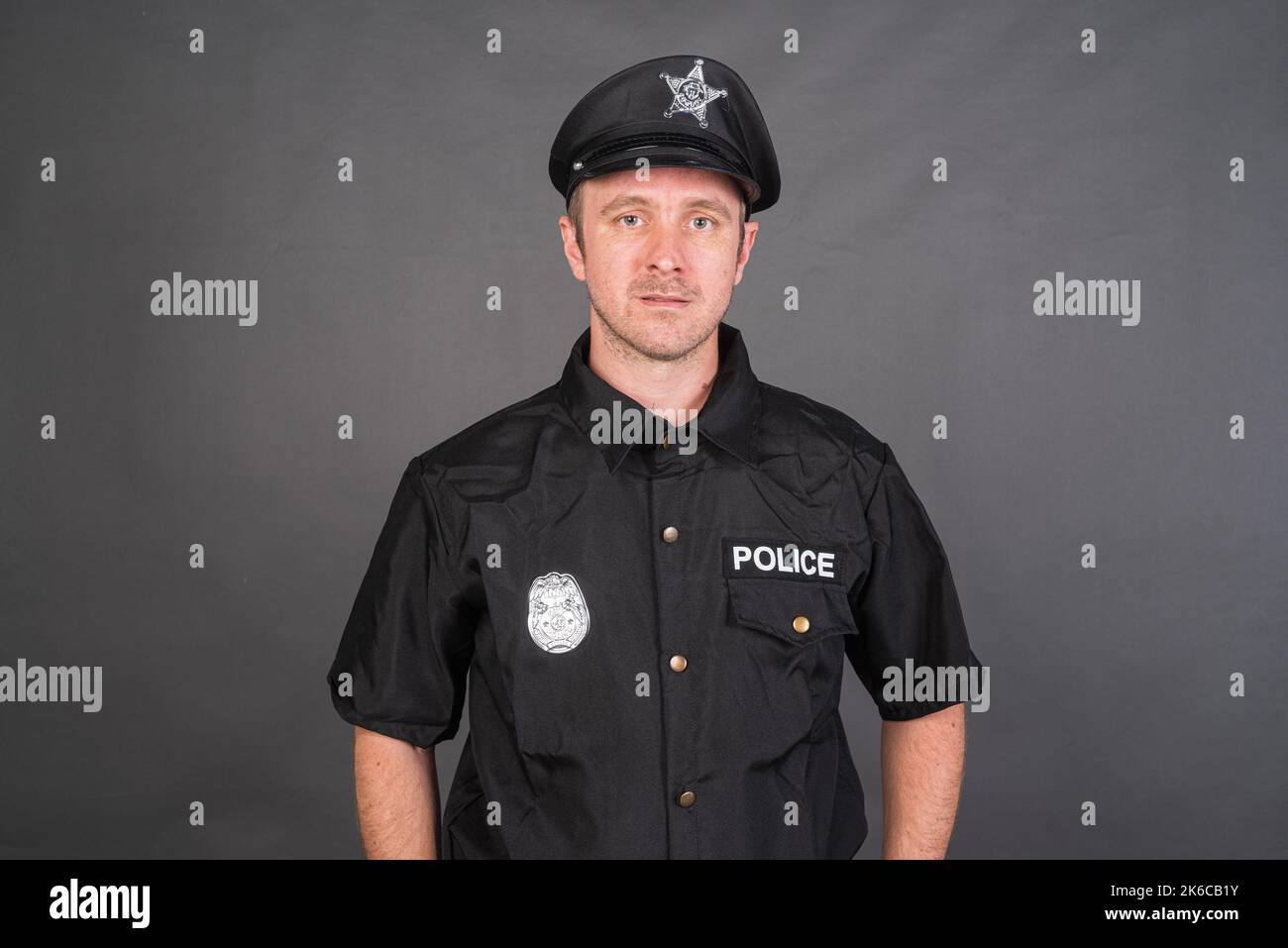Portrait d'un homme de race blanche portant un costume de police sur fond gris de studio Banque D'Images