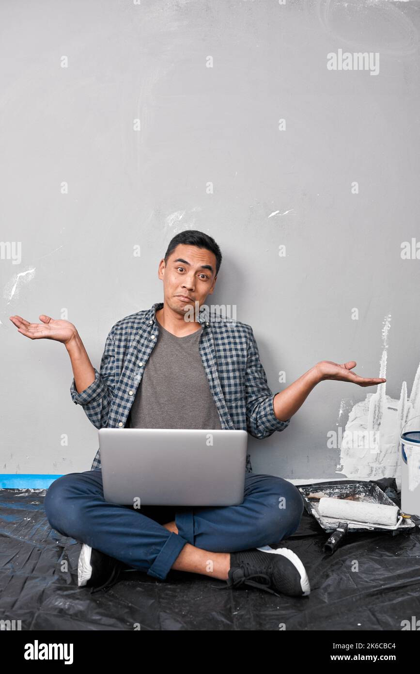 Un jeune homme asiatique se fait l'effet d'ignorer le bricolage et la rénovation de sa maison avec son ordinateur portable Banque D'Images