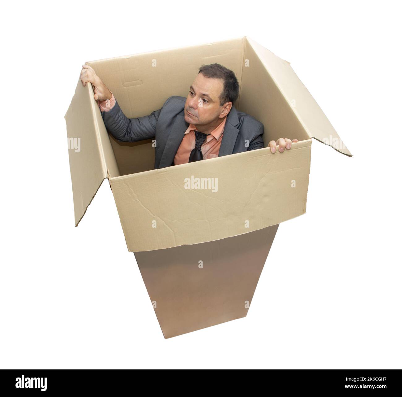 Un homme en costume se tient à l'intérieur d'une boîte en carton et essaie de regarder dehors, isolé sur fond blanc Banque D'Images