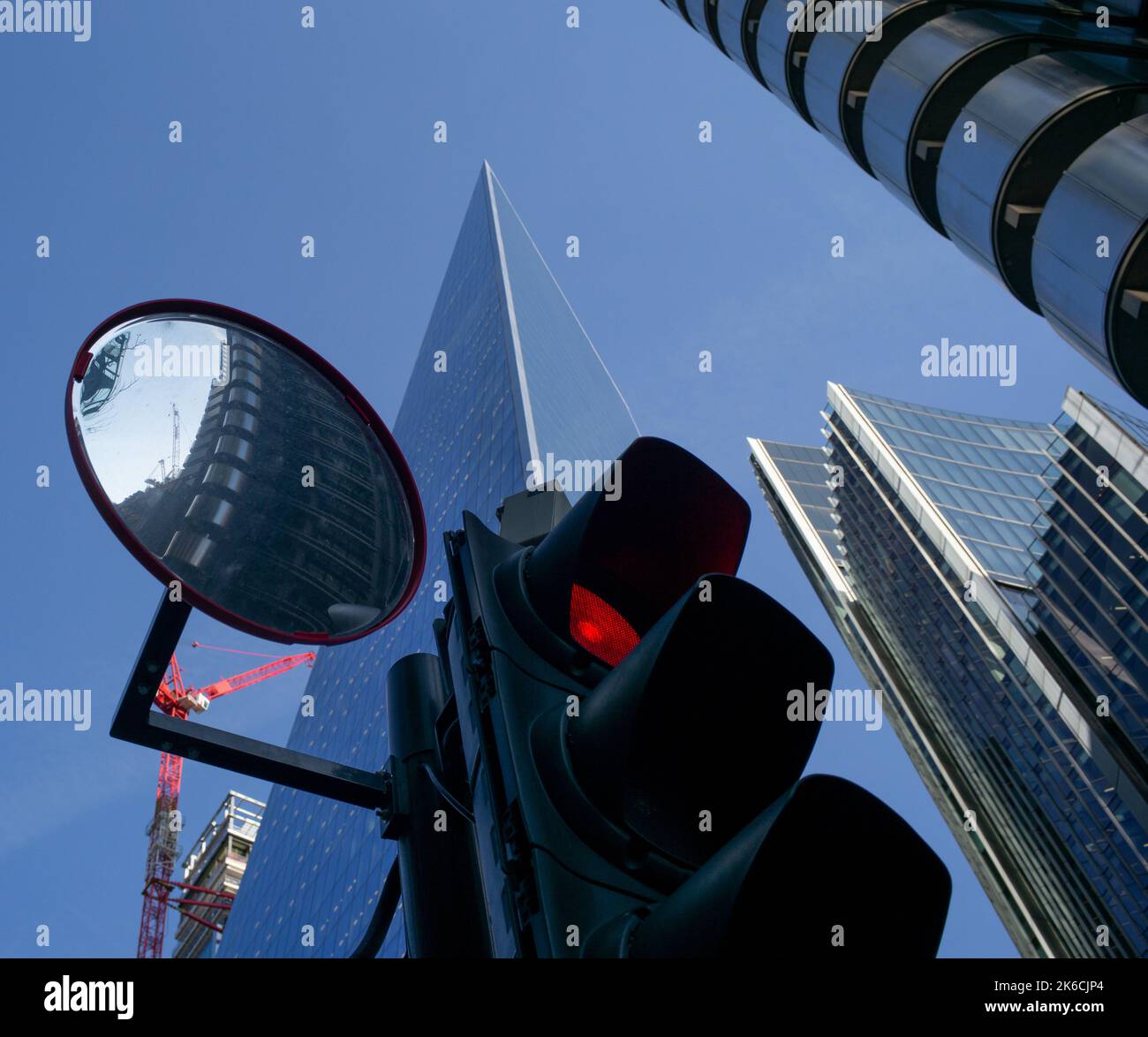 Image conceptuelle d'un gros plan d'un feu rouge avec un miroir de signalisation reflétant le bâtiment Lloyds et les gratte-ciels en arrière-plan. Banque D'Images