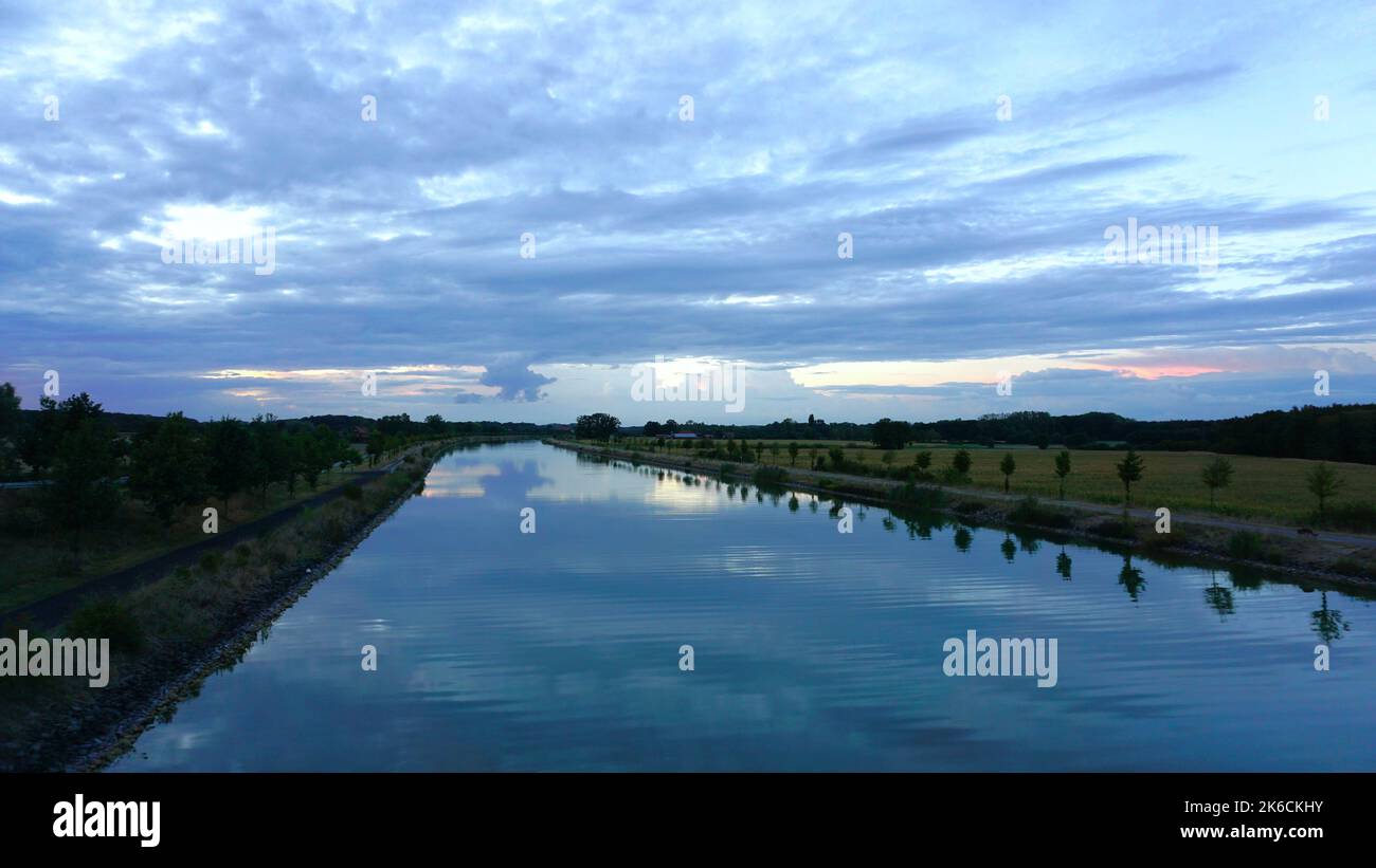 Un coucher de soleil nuageux sur le canal EMS de Dortmund avec des arbres alignés sur la rive de la rivière Banque D'Images